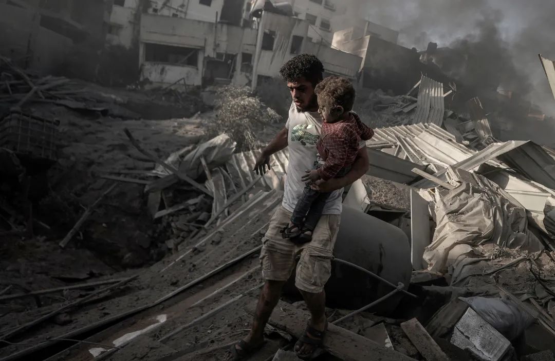 当地时间2023年10月25日,加沙地带,一名巴勒斯坦人抱着孩子走在以色列