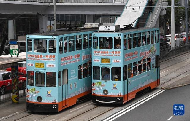 12月1日，两辆涂有2023年区议会一般选举宣传广告的电车从香港街头驶过。新华社记者 陈铎 摄