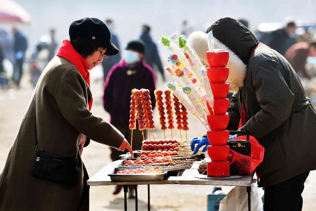 2月14日,在山东省青岛市城阳区河套街道正月首个大集上,市民在摊位前