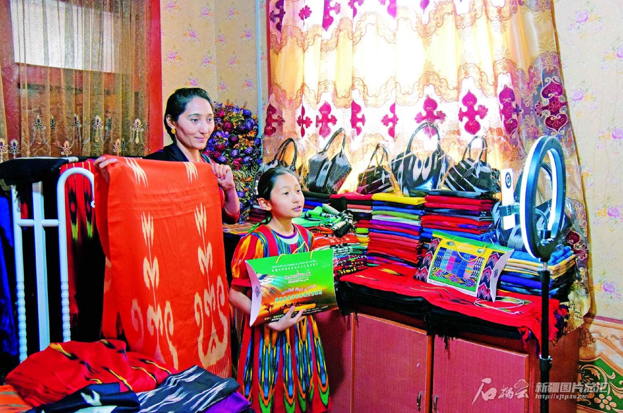 在洛浦县布亚乡阿亚格夏合勒克村，村民努尔古丽·图尔荪托合提（左）正在家中直播销售自己生产的艾德莱斯产品。 张亚辉摄
