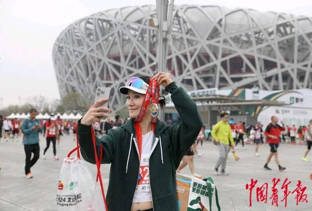 4月14日，北京国家体育场“鸟巢”前，一位结束比赛的女跑者手持奖牌拍照留念。中青报·中青网记者 陈剑／摄