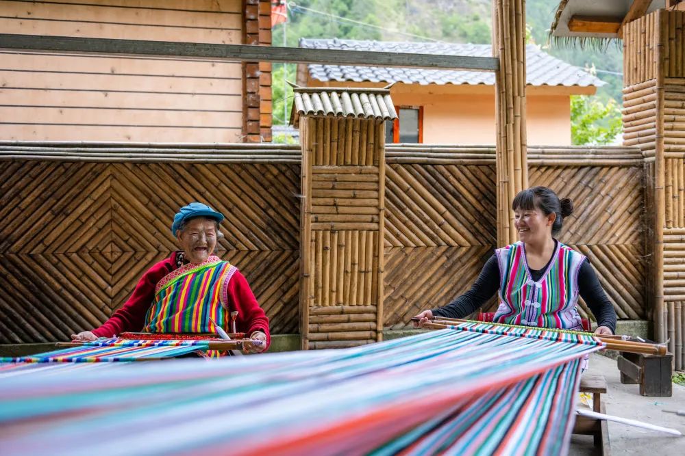 2022年5月10日，在独龙江乡迪政当村，独龙族老人李文仕（左）和女儿在编织独龙毯。曹梦瑶 摄