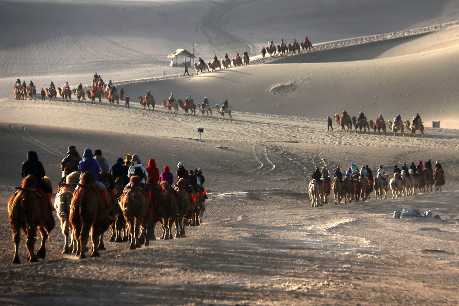 2024年4月24日，甘肃省敦煌市，游客骑骆驼在鸣沙山月牙泉景区游览。