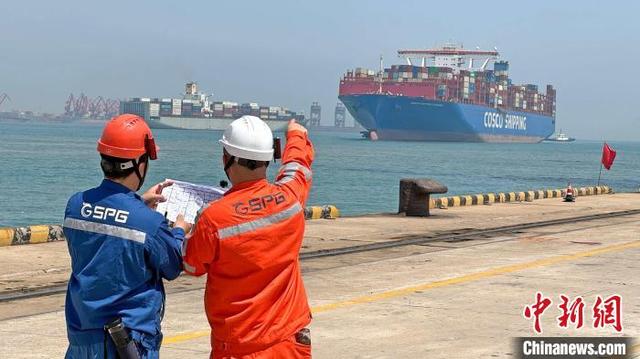 5月1日，两名工人在山东港口青岛港码头上协助巨轮靠泊。薛景文 摄
