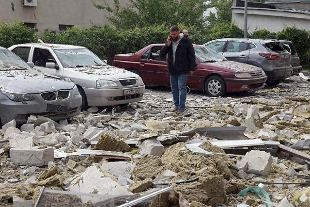当地时间2024年5月14日，乌克兰哈尔科夫，一名男子在被俄罗斯炮击受损的多层住宅外的汽车残骸旁打电话。视觉中国 图