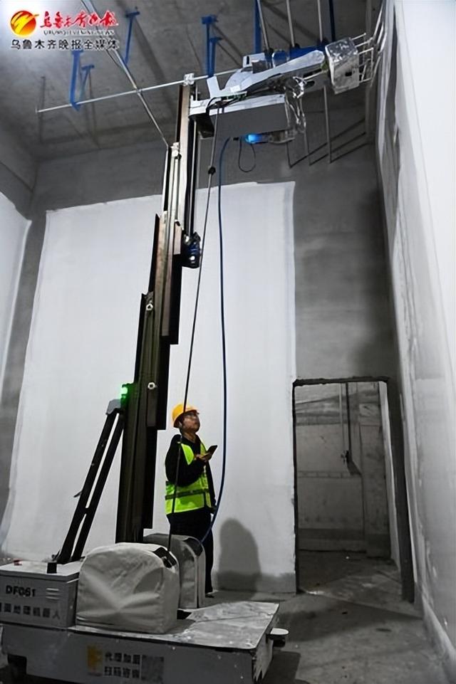 建设工地,工作人员使用手机操控墙面处理机器人对墙体进行喷涂作业