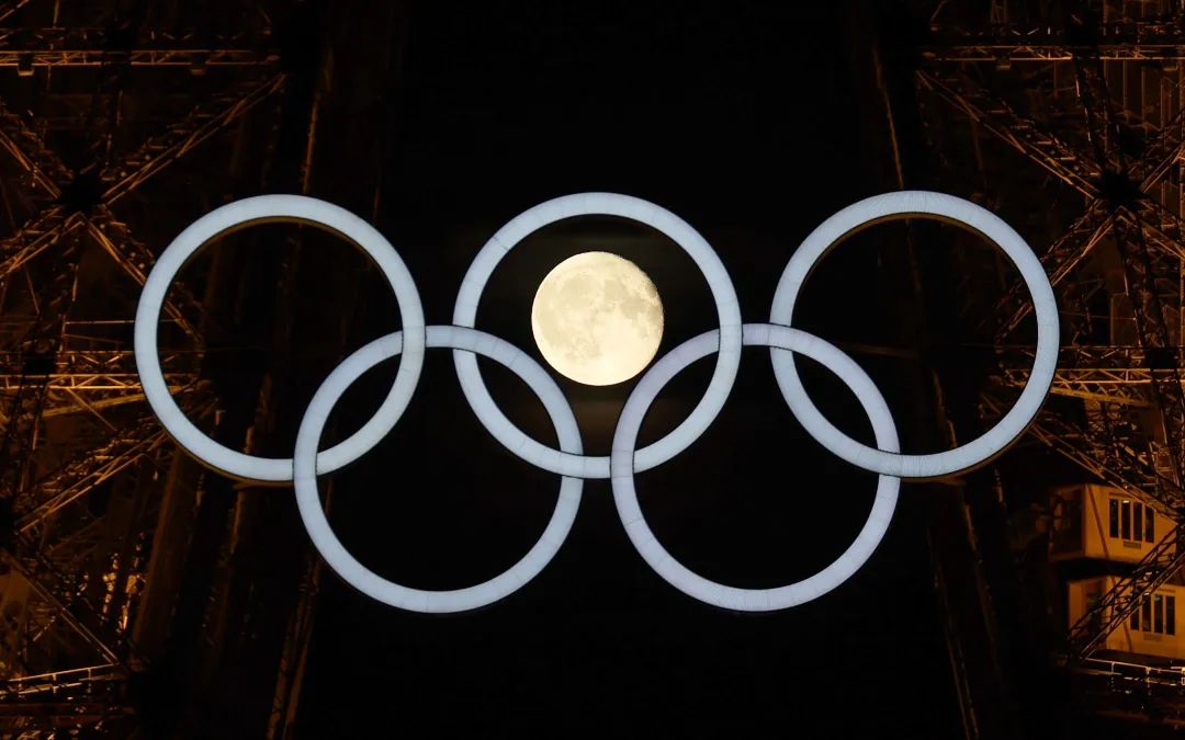 ▲当地时间7月23日凌晨，一轮圆月“现身”悬挂在埃菲尔铁塔上的奥运五环中。图/新华社