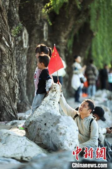 10月2日，国庆黄金周第二天，北京北海公园吸引游客。图为家长协助小朋友与国旗合影。中新社记者 张祥毅 摄