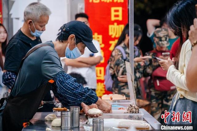 “锅盔叔叔”胡伟光(左二，戴帽子)正在为顾客制作锅盔。李南轩 摄