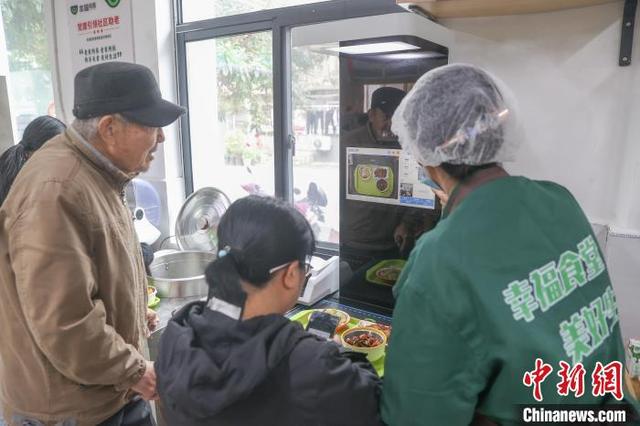 11月21日，在位于江西南昌东湖区的光明社区幸福食堂，工作人员协助民众使用智能结算设备付款。中新社记者 刘力鑫 摄