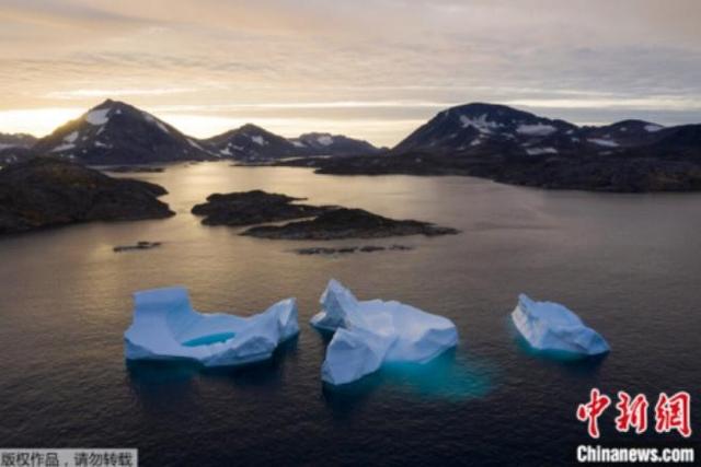 资料图：日出时，格陵兰岛附近的一座大型冰山正在漂走。