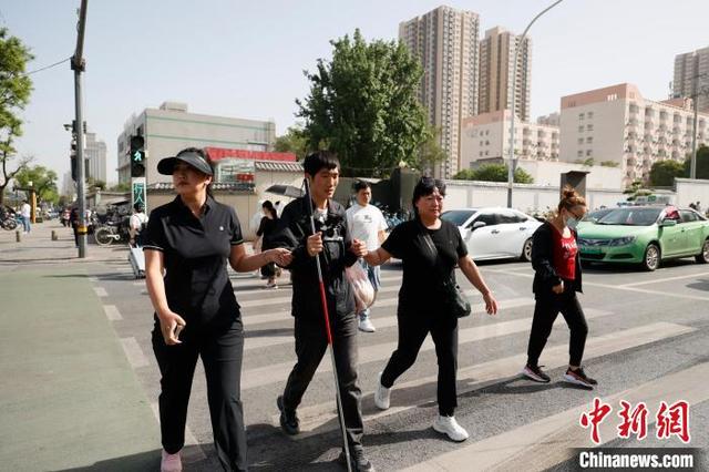 图为爱心人士协助谭维乐过斑马线。 梅镱泷 摄