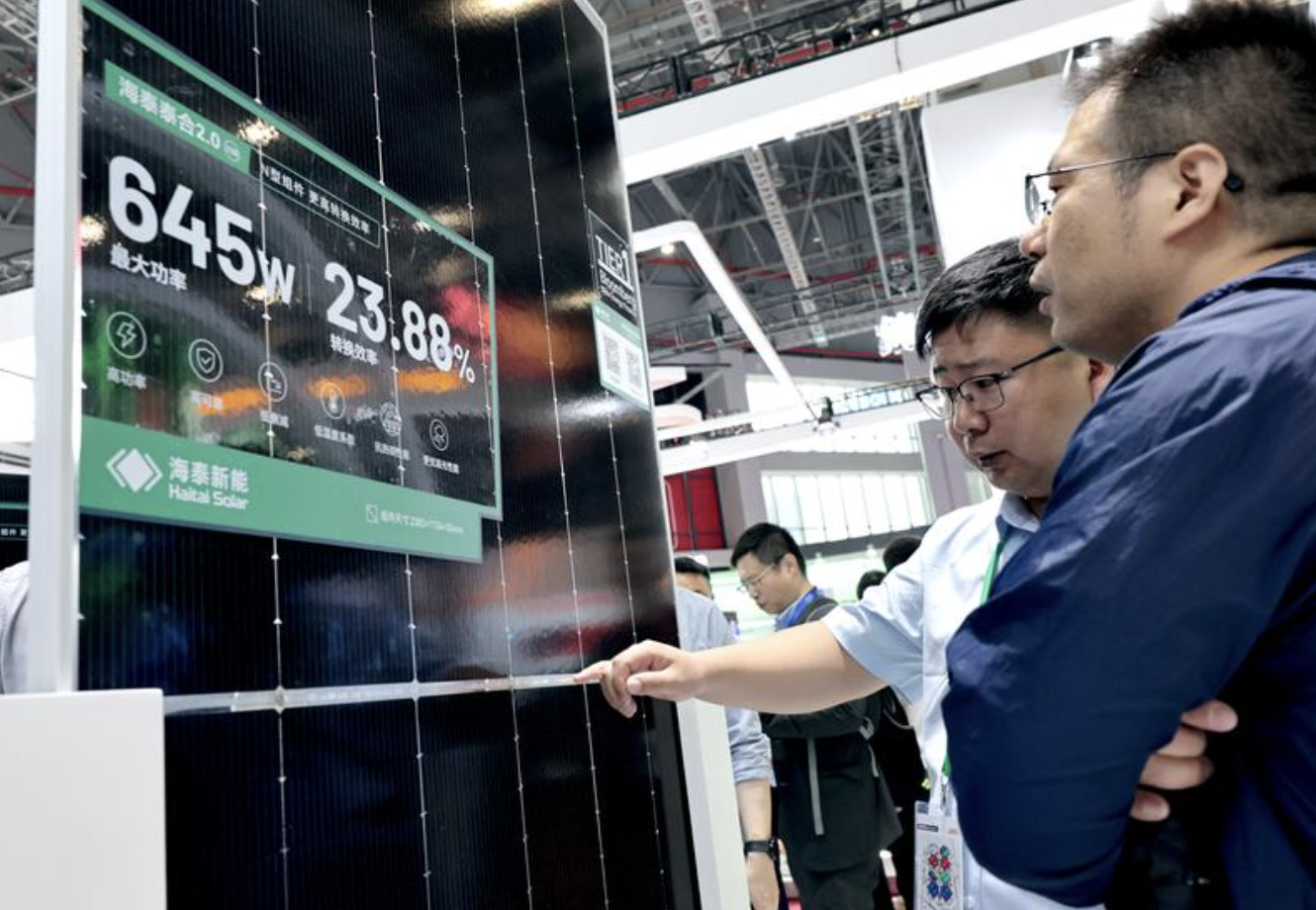 （今年6月举办的2025上海光伏展上，参观者在一个沙漠光伏组件展品前交流讨论。图片来源：新华社）