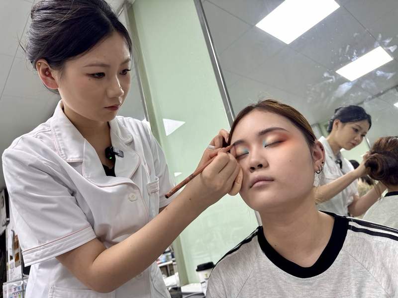 崔家慈（左）给模特化妆。新京报记者 耿子叶 摄