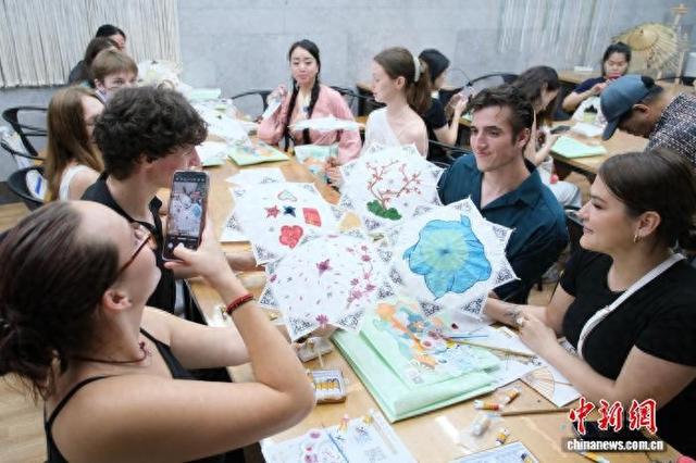 2025年6月，外国青年在浙江杭州的中国刀剪剑博物馆内与自己绘制的扇面合影留念。曹丹 摄