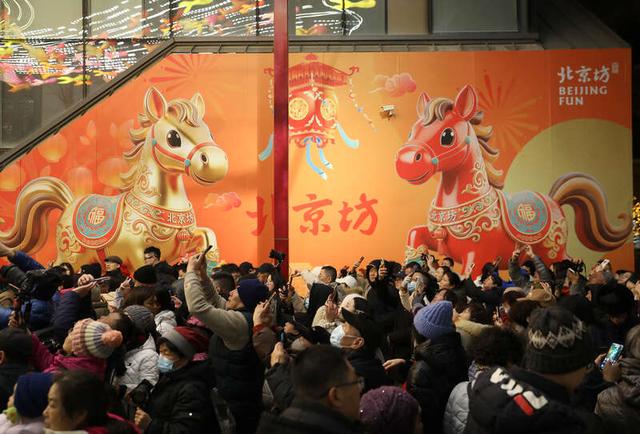 2月15日晚，位于北京前门大街旁的廊房头条，在巨幅生肖马年海报旁，游客正在花灯下拍照。中青报·中青网记者 陈剑/摄