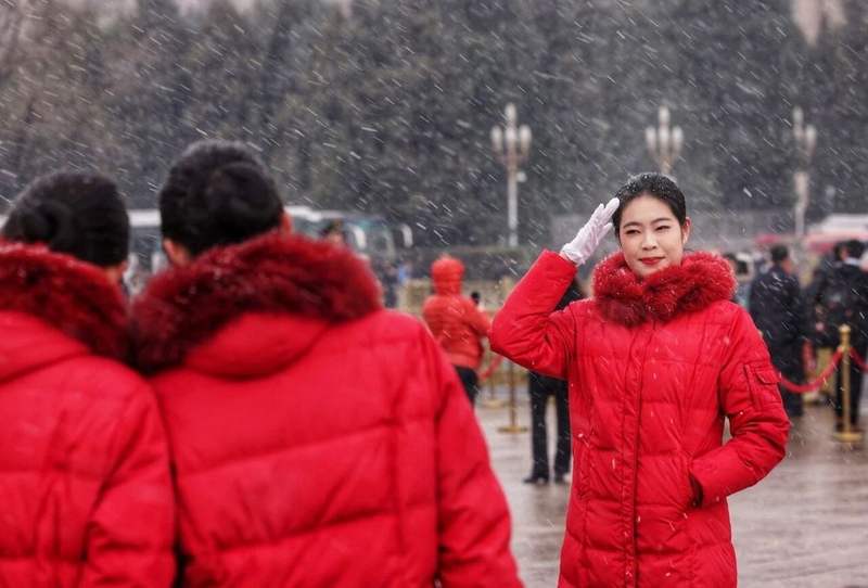 3月4日，身着红衣的会议服务人员在瑞雪中拍照。