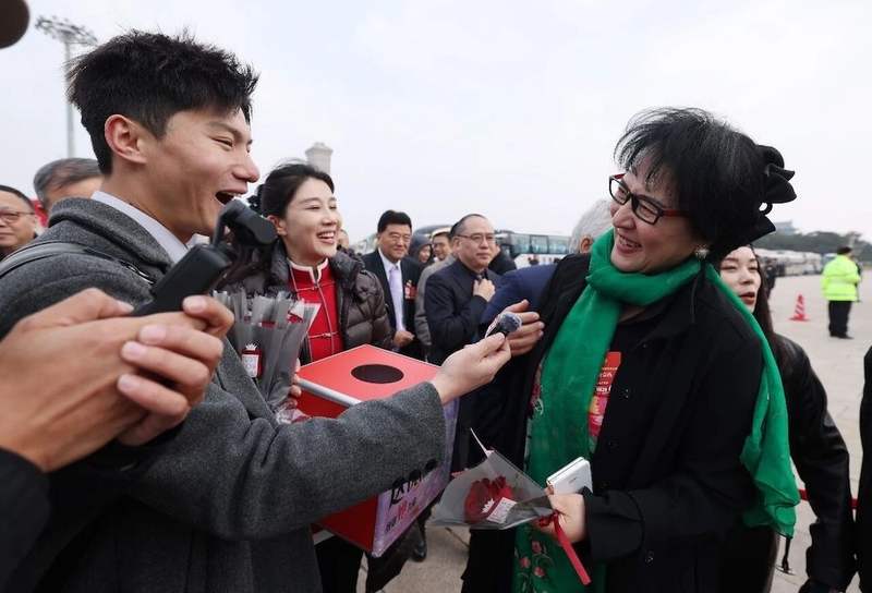 3月7日，天安门广场，全国政协十四届四次会议第二次全体会议前，一名女政协委员接受媒体赠送的鲜花并接受采访。