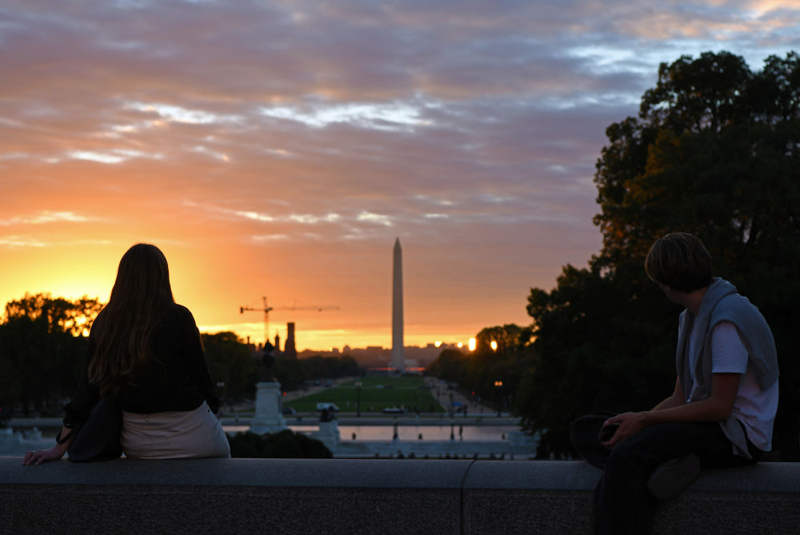 2025年10月15日，在美国华盛顿，人们在国会大厦前观看日落时分的华盛顿纪念碑。新华社记者李睿摄