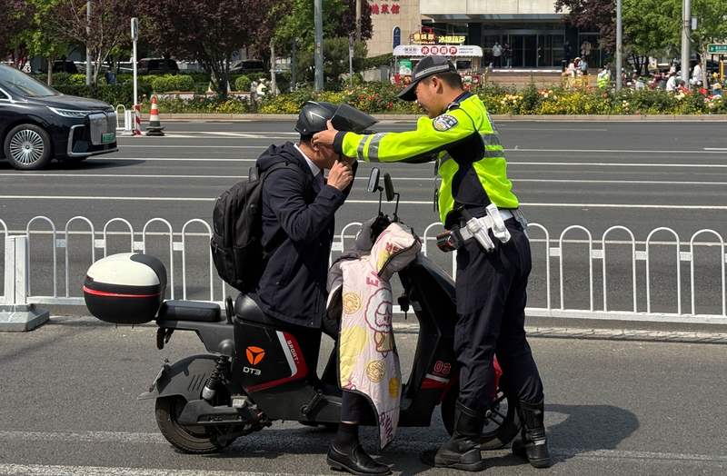 执勤交警现场指引一位市民按照规范戴好头盔，不能只携带而不佩戴。新京报记者 王贵彬 摄