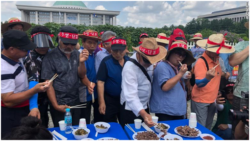 (狗農協會的多名狗肉業者當場大口吃起狗肉。圖源:CNN)