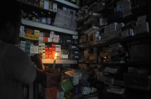  图为在印度西里古里，一位药店店员借着烛光寻找药品。新华社/法新