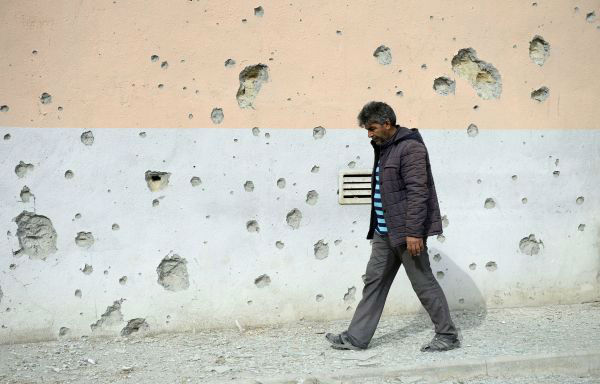  9月29日，在阿塞拜疆临近纳卡边境的塔塔尔地区，一名村民从布满弹孔的墙壁旁经过。新华社发
