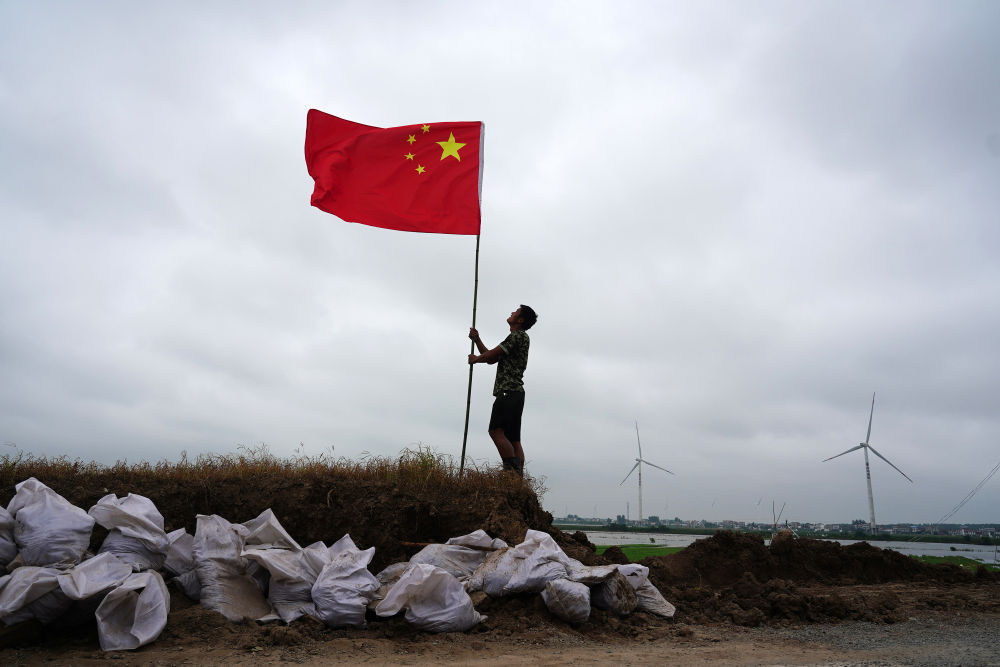 7月16日,在江西省九江市,退役军人张恒扶正防洪哨所门前的国旗。洪水来袭,曾服役于天安门国旗护卫队的张恒同父亲一起投身防汛抗洪战斗。他说,过去我护卫的是国家的荣誉和尊严,现在我守卫的是父母和家乡。新华社记者 周密 摄
