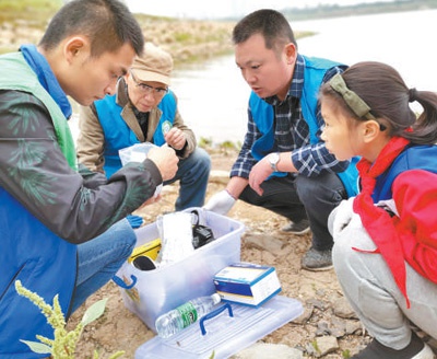 湖南湘潭市民间河长张一彬（左一）在湘江沿岸的唐兴桥排污口指导市民做简易水质检测。 　　沈雪梅摄
