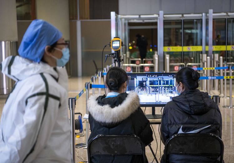 首都国际机场，防疫人员和工作人员通过体温检测设备对抵京旅客进行体温检测。
