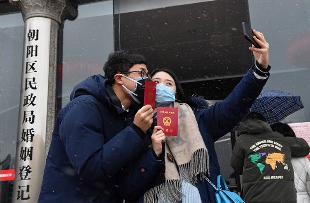  领完结婚证的一对新人站在雪中，戴着口罩自拍合影。新京报记者 李木易 摄