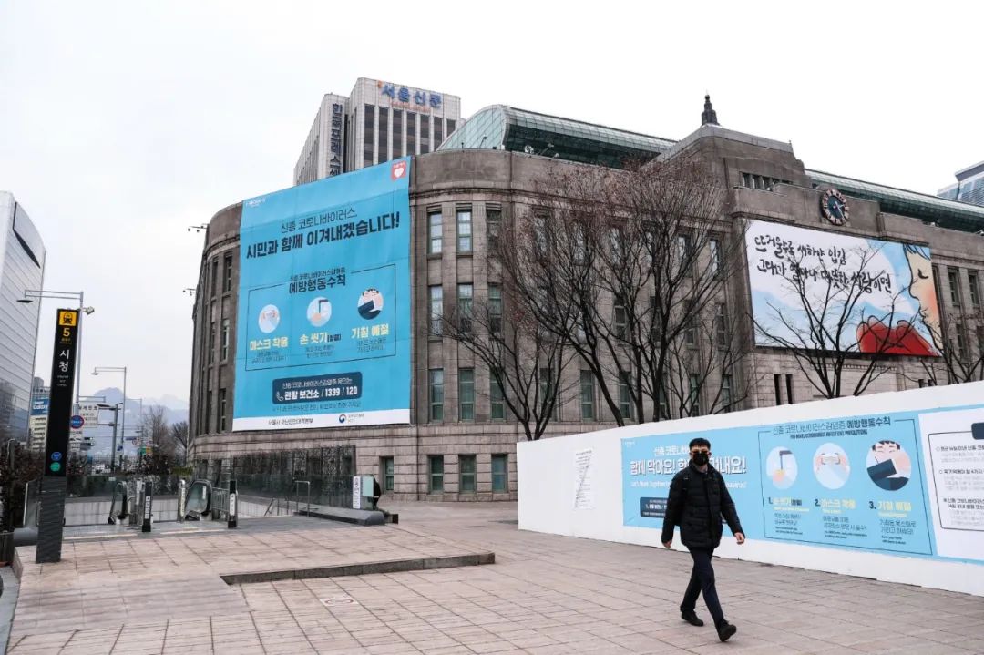 2月21日，一名男子从韩国首尔市政府挂出的巨型“新冠病毒预防要领”宣传海报旁边经过。新华社记者 王婧嫱 摄