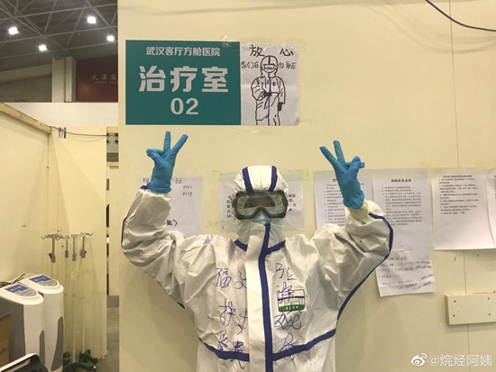 2月18日，武汉客厅方舱医院，一名福建医疗队护士。她身后的墙上贴着一张医护人员的卡通漫画，上面写着：“放心，我们在你身后。”@烷烃阿姨