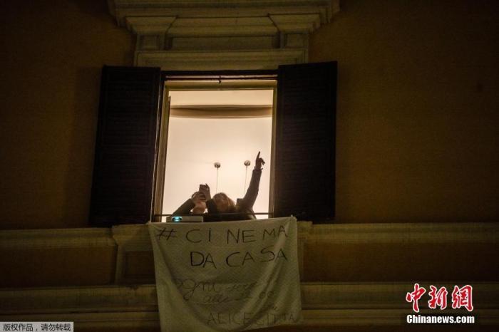 资料图：意大利罗马，Fabia Bettini对儿子指着街对面建筑上投放的电影《西班牙广场的女孩》。这也是罗马电影节的活动之一，旨在鼓励民众在意大利新冠病毒疫情期间留在家中。