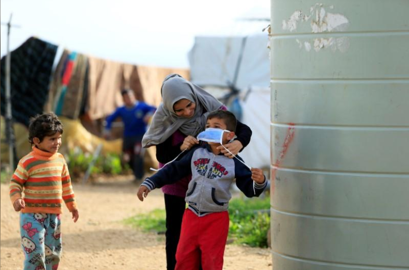 ▲当地时间3月20日，在黎巴嫩南部的Al-Wazzani地区一处难民营，一位难民母亲给孩子戴上了防护口罩。图据路透社