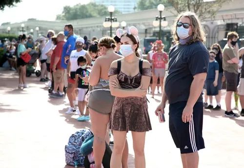  7月11日，游客戴着口罩在美国奥兰多华特迪士尼世界的神奇王国主题乐园外排队。新华社/法新