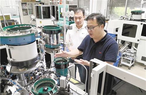 图为华圣达研发人员（右）介绍自主研发的智能生产拉链设备。本报记者 杨阳腾摄
