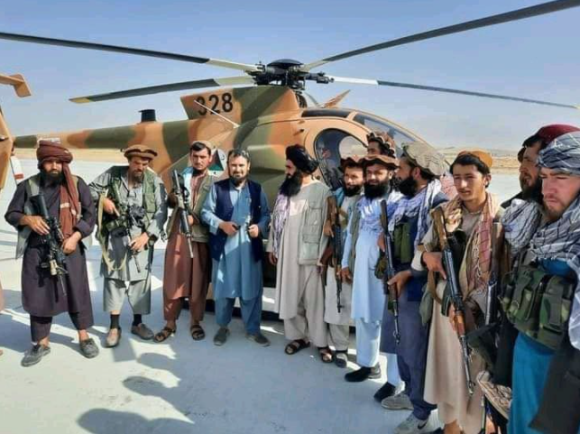 Taliban personnel take a group photo in front of the US-made MD-530 helicopter