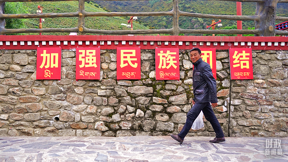 △西藏林芝嘎拉村村民走过“加强民族团结”标语墙。（总台国广记者李晋拍摄）