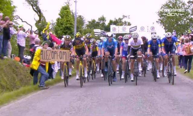 事故发生前，这名女子在环法自行车赛选手面前举着牌子（英国卫报报道截图）