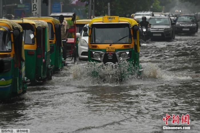 资料图：当地时间9月11日，印度新德里，一场暴雨过后路面积水严重，民众驾车驶过溅起水花。