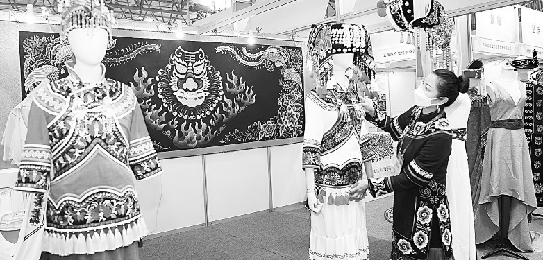 创意云南2021文化产业博览会日前在昆明举行。图为博览会期间，商家在创意云南2021文化产业博览会上整理民族服饰。