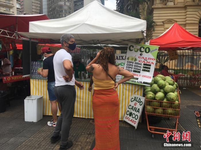 当地时间10月3日，巴西圣保罗，市民在街头集市购买椰子水饮料。目前，目前，随着当地新冠疫情趋缓，巴西最大城市圣保罗街头集市已恢复如常，顾客增多，生意渐旺。 中新社记者 莫成雄 摄