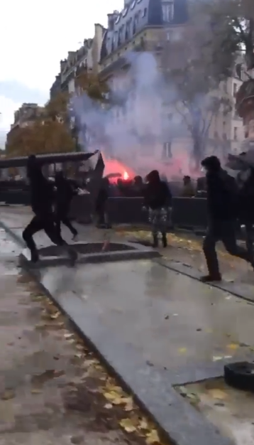 法国街头，黑衣人举起金属路障追打警察