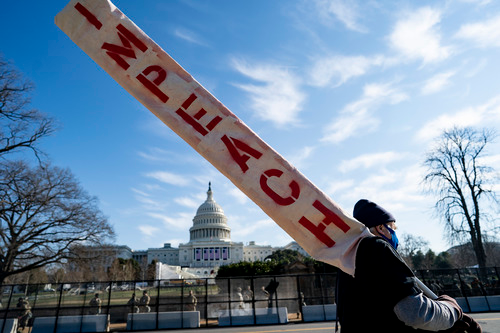 1月13日，在美国首都华盛顿，一名手持“弹劾”标语的男子从国会大厦前走过。新华社记者刘杰摄