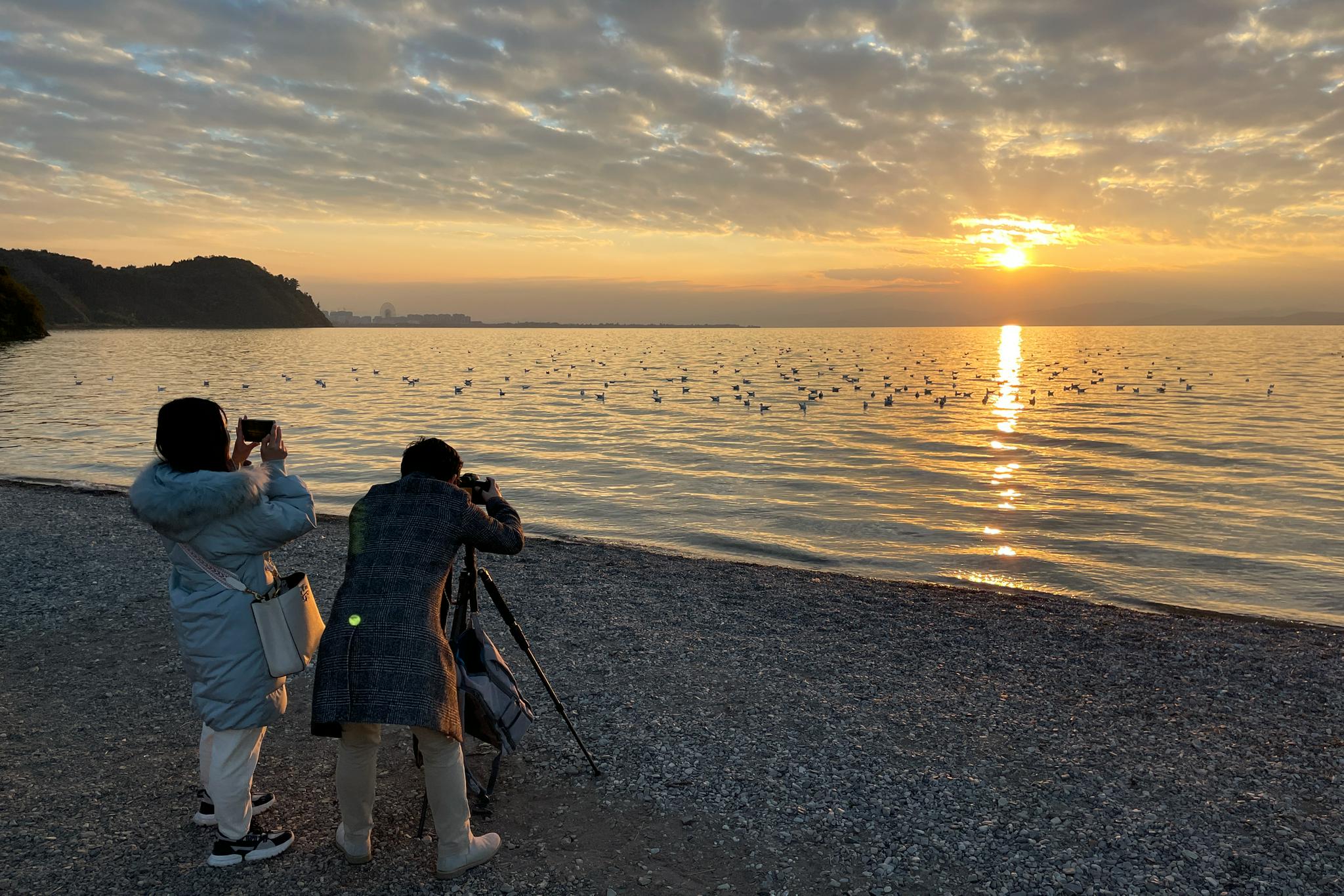 11月30日，游客在海晏村滇池畔拍摄日落。（中国日报记者 武晓慧 摄）