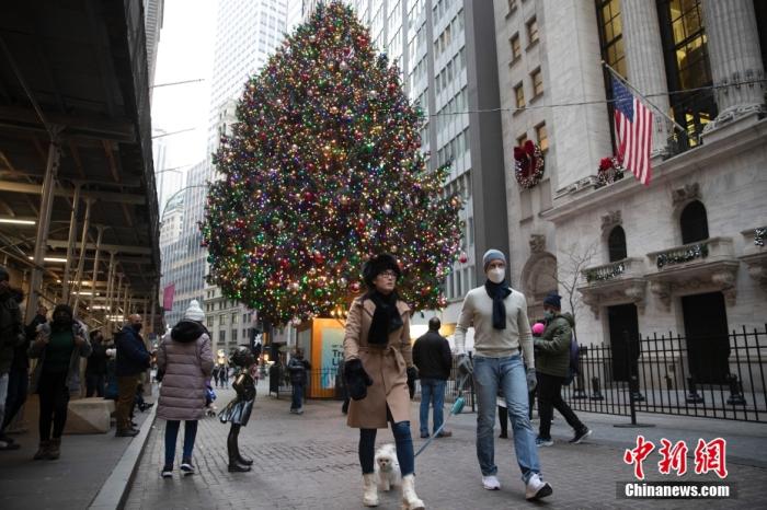 资料图：当地时间12月24日，人们经过美国纽约华尔街上布置的一棵圣诞树。在新一轮新冠肺炎疫情中，当地迎来圣诞节平安夜。 中新社记者 廖攀 摄