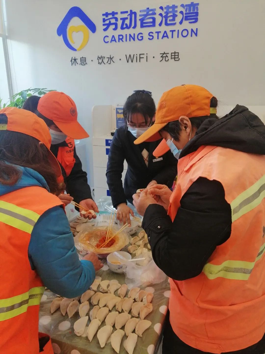 图为建设银行江苏镇江北固湾支行的网点员工邀请外地环卫工人在网点一起包饺子。