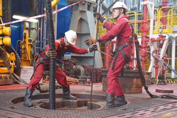 钻井班组正在进行吊装电缆作业,几个钻工铆劲拉拽尾绳,确保电缆安全下