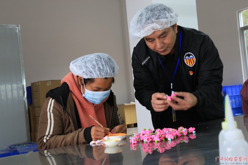 罗旺彬（右一）到村里的工业扶贫基地了解脱贫户加工玩具生产情况